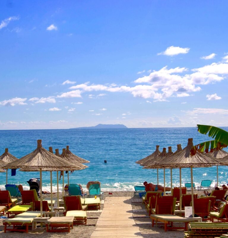 Relaxing summer day at Dhërmi beach, Albania with turquoise sea, umbrellas, and sun loungers.