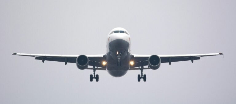 A commercial airliner captured head-on, preparing to land against a cloudy sky.